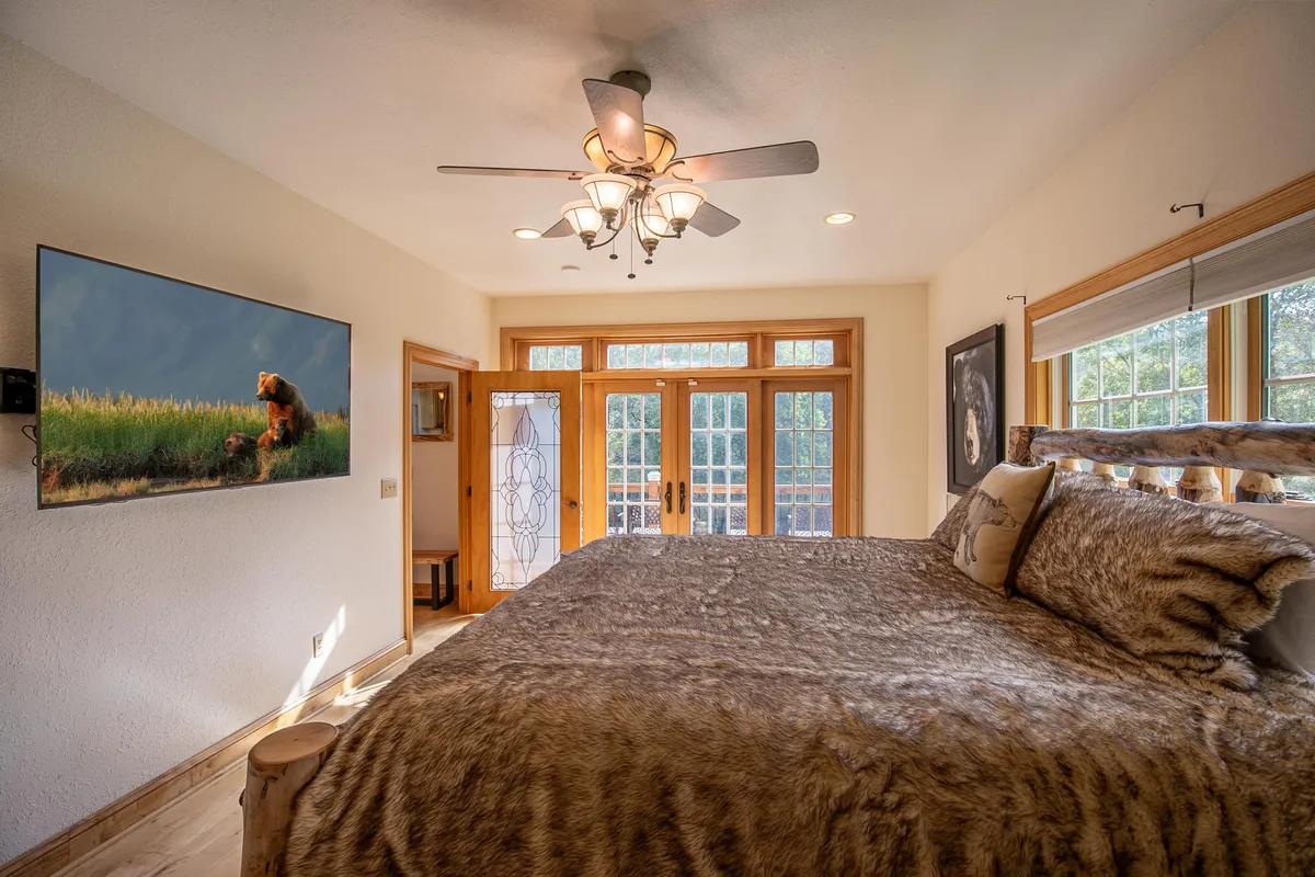 This image features a king-sized bed adorned with a fur throw, large windows inviting abundant natural light, and a wall decorated with bear artwork. The tranquil, comfortable mood is enhanced by soft textures and an inviting atmosphere, perfect for relaxation.