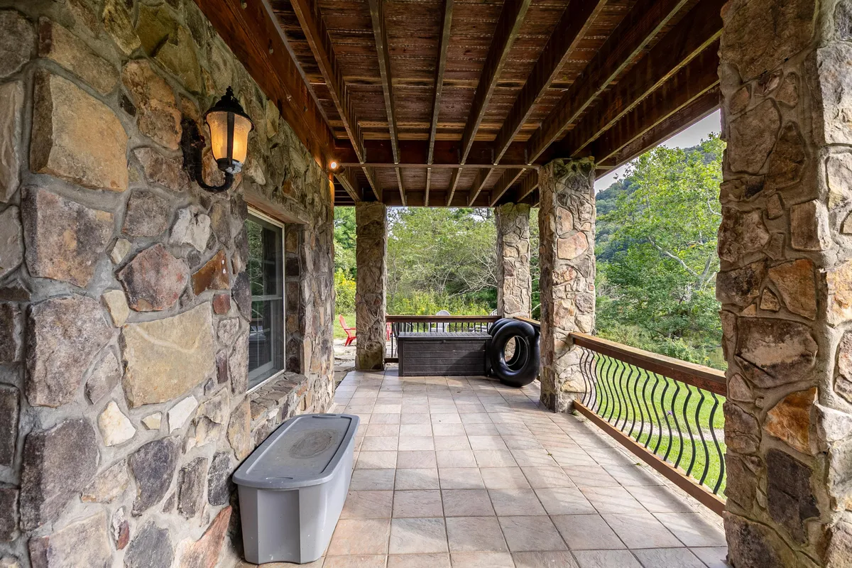 A rustic stone porch with wooden beams and warm lantern light, offering a cozy, sheltered spot to take in the surrounding greenery. The porch feels both private and inviting, evoking evenings spent relaxing or gathering with friends.
