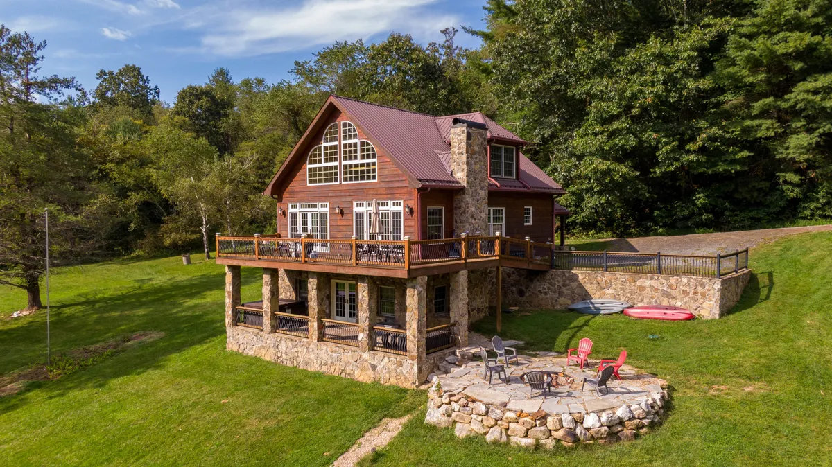 This exterior image displays the house with a welcoming stone patio, surrounded by green lawn and trees. The space is ideal for outdoor gatherings or games, with the nearby water suggesting opportunities for kayaking or riverside picnics under the open Carolina sky.