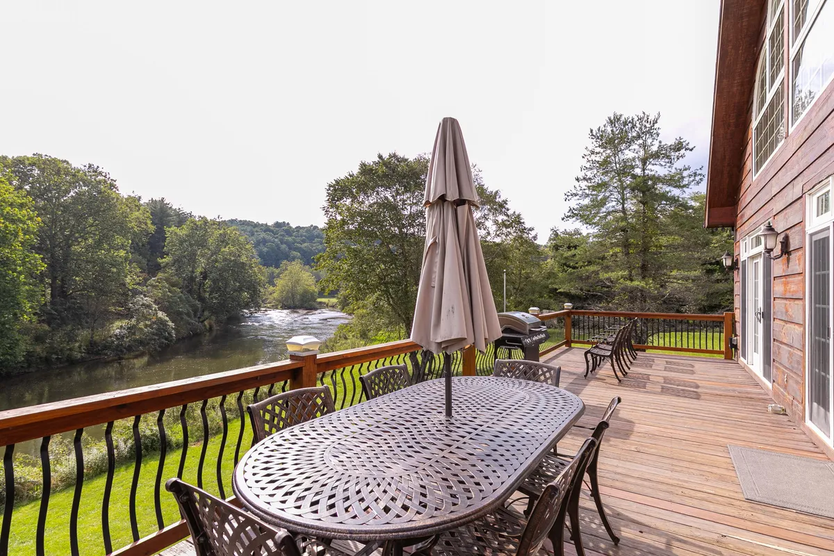 A tranquil outdoor dining setup on a spacious deck, overlooking the river and framed by lush green foliage. The setting is ideal for al fresco meals, socializing, and enjoying the sights and sounds of nature in warmer months.