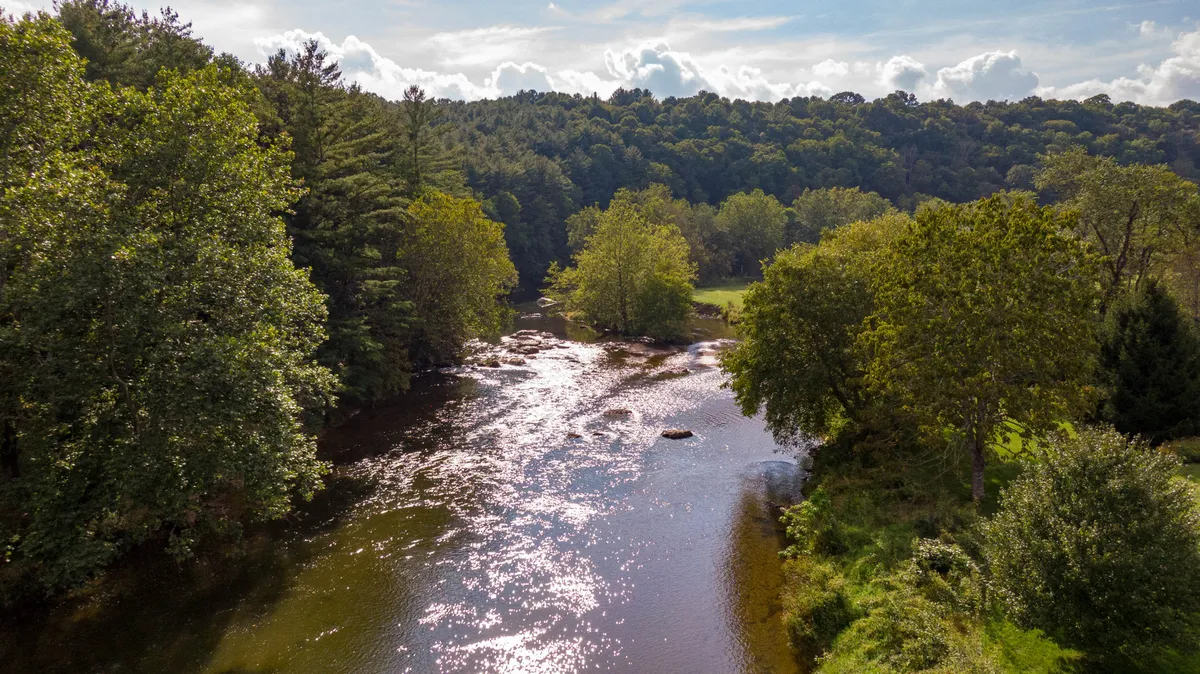 A wide, flowing river bordered by lush greenery and framed by distant hills, offering a serene, natural escape. The peaceful setting highlights the river access and nearby trails mentioned in the section.