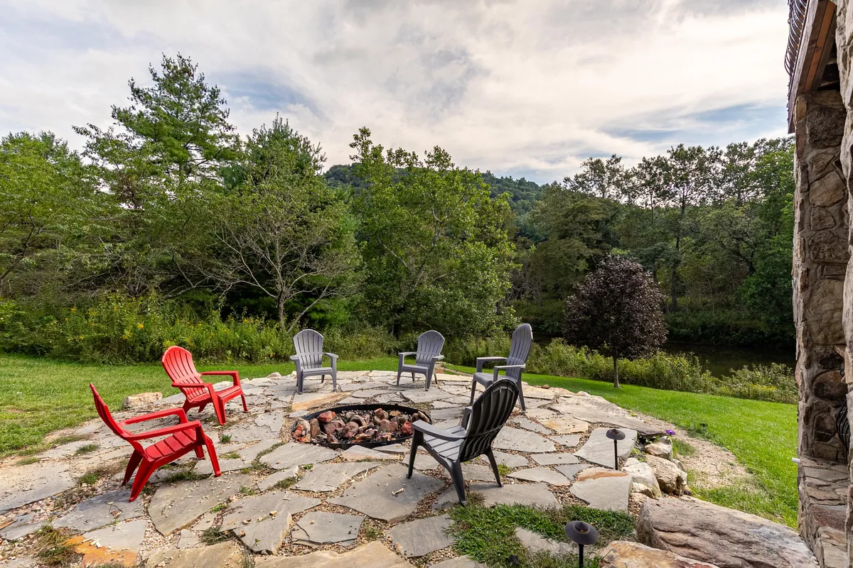 This image highlights a cozy fire pit surrounded by comfortable seating and nestled in natural surroundings. The setup encourages gatherings, storytelling, and warmth under the open sky, with trees and greenery providing a serene backdrop.