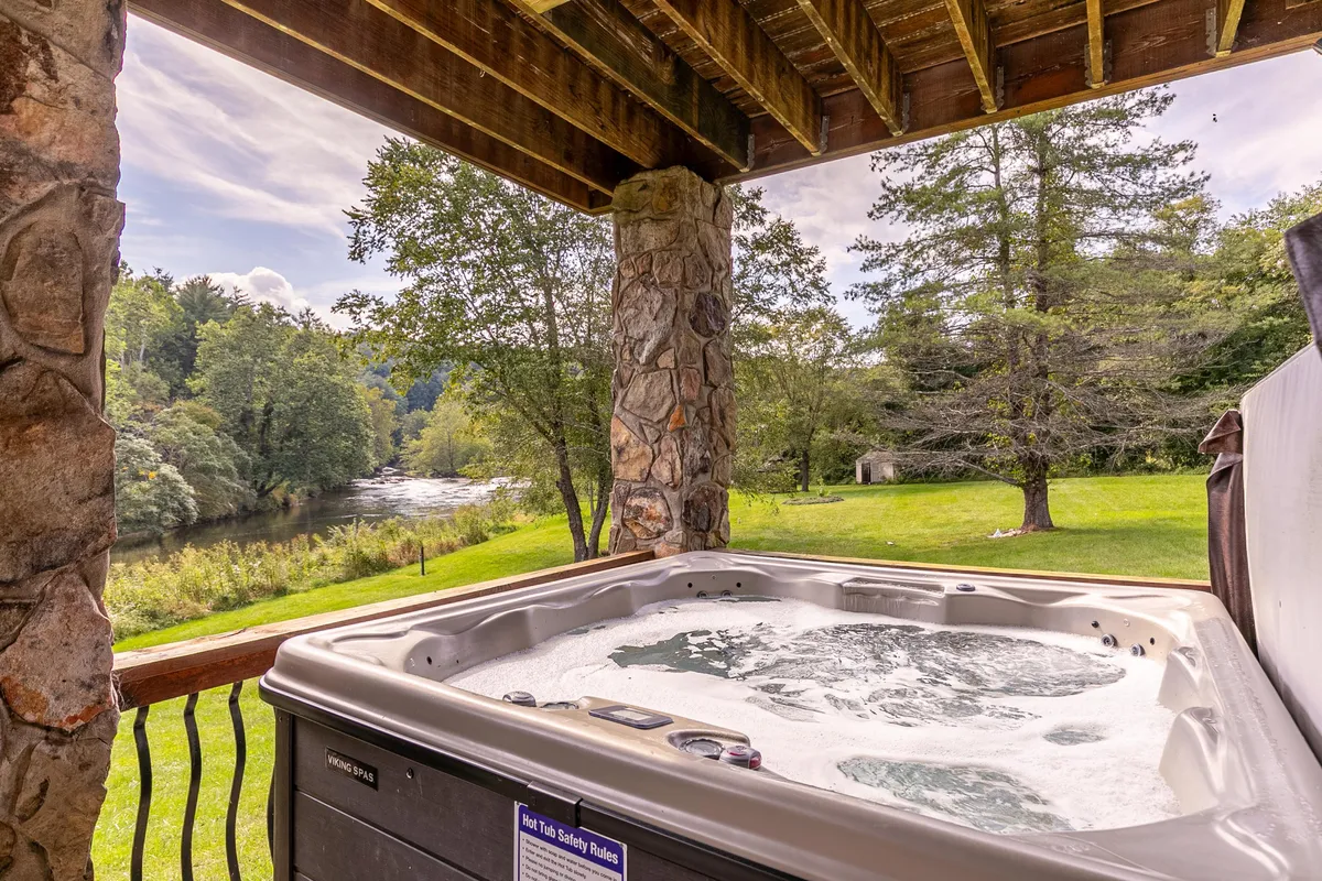 This exterior image features a luxurious hot tub perched with a direct view over the river, framed by stone pillars. The tranquil setting invites relaxation, with the water just steps away and natural beauty all around. The scene suggests both daytime and evening enjoyment, perfect for unwinding after river adventures.